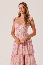 A woman is wearing a pink floral dress with ruffled cap sleeves, a sweetheart neckline, and a fitted bodice. The dress features a tiered skirt with multiple layers that have a ruffled edge. The fabric has a pattern of green and yellow leaves and pink flowers.